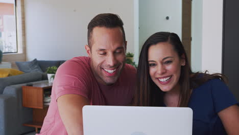 una pareja hispana en casa con una computadora portátil hablando por video con la familia.