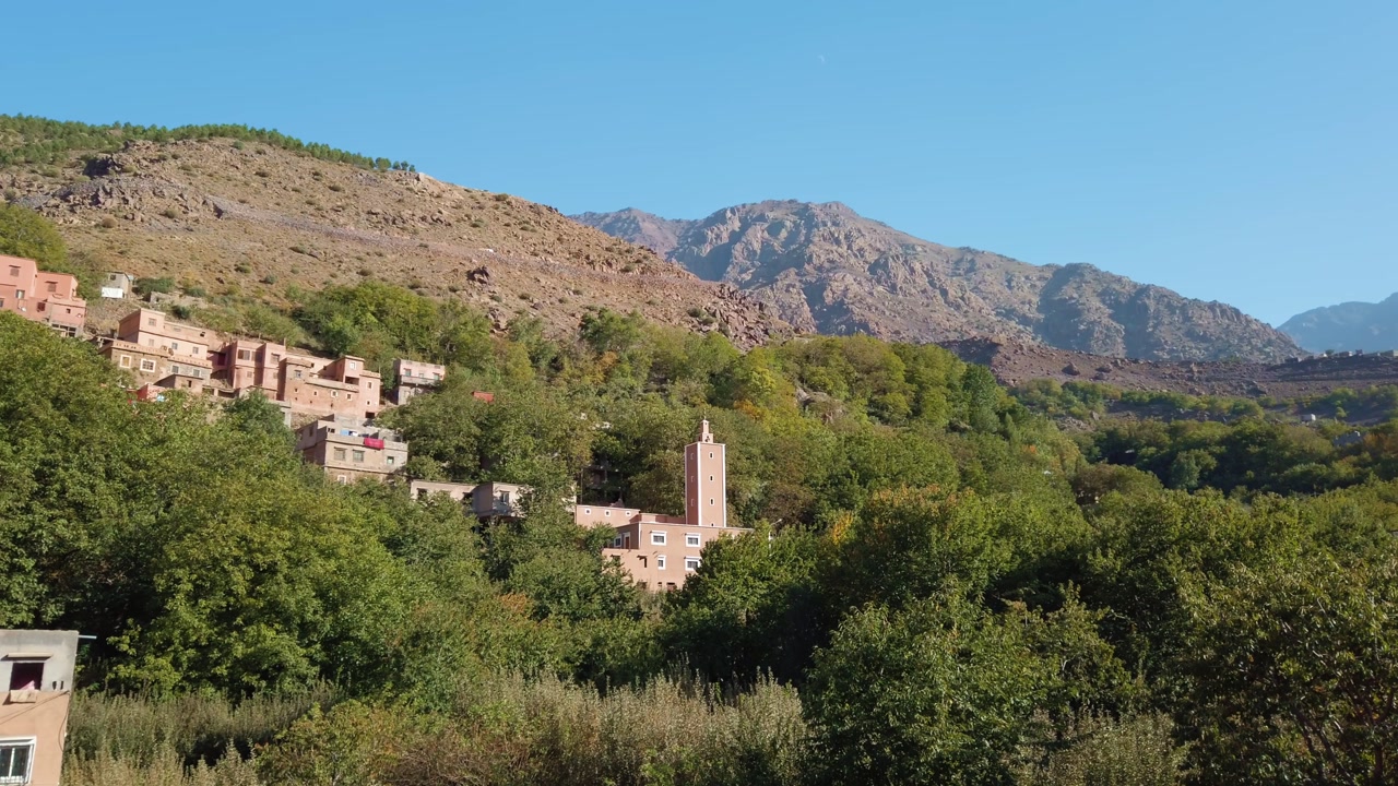 Imlil, a Berber mountain village in Morocco’s High Atlas Mountains near Toubkal National Park, features traditional architecture amid rocky hillsides, and clear blue sky in an elevated panoramic view.