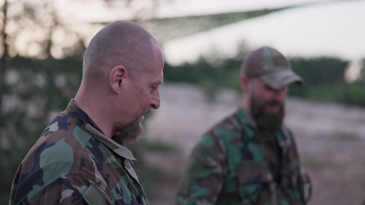 conversación de soldados en ropa de camuflaje, están discutiendo por la noche junto a la fogata común fritando salchichas para la cena, los hombres están descansando después del trabajo, servicio, ejercicios de campo