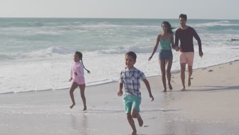 happy hispanic mother, father, son and daughter running on beach