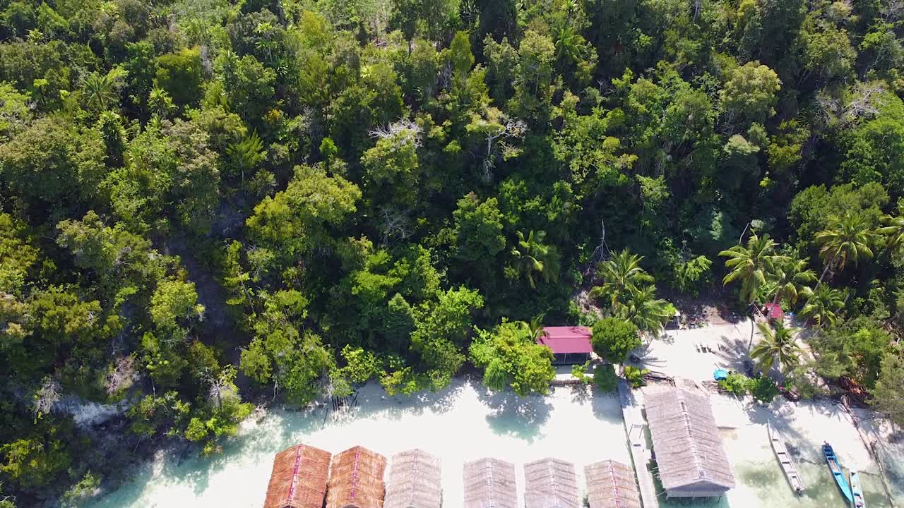 aerial que se eleva sobre la remota cabaña de playa con vistas al arrecife de coral y el agua cristalina del océano en raja ampat, papúa occidental, indonesia