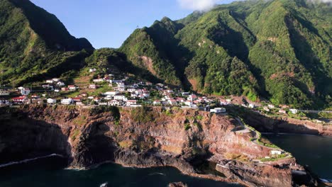 aerial view of a town on a volcanic rocky cliff on epic green madeira coast