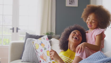 mother and daughter relaxing on sofa at home reading book together