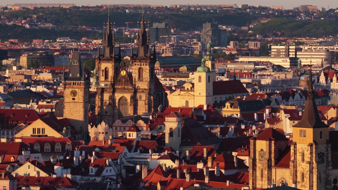 Vista aerea con drone che guarda su fitti tetti di tegole rosse del centro storico con le doppie guglie gotiche della Chiesa di Tyn che dominano lo skyline durante la calda ora d'oro