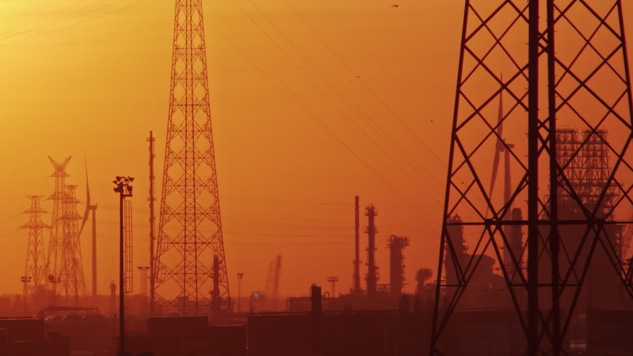 Large electricity pylon dominates hazy industrial skyline with distillation columns and turbines