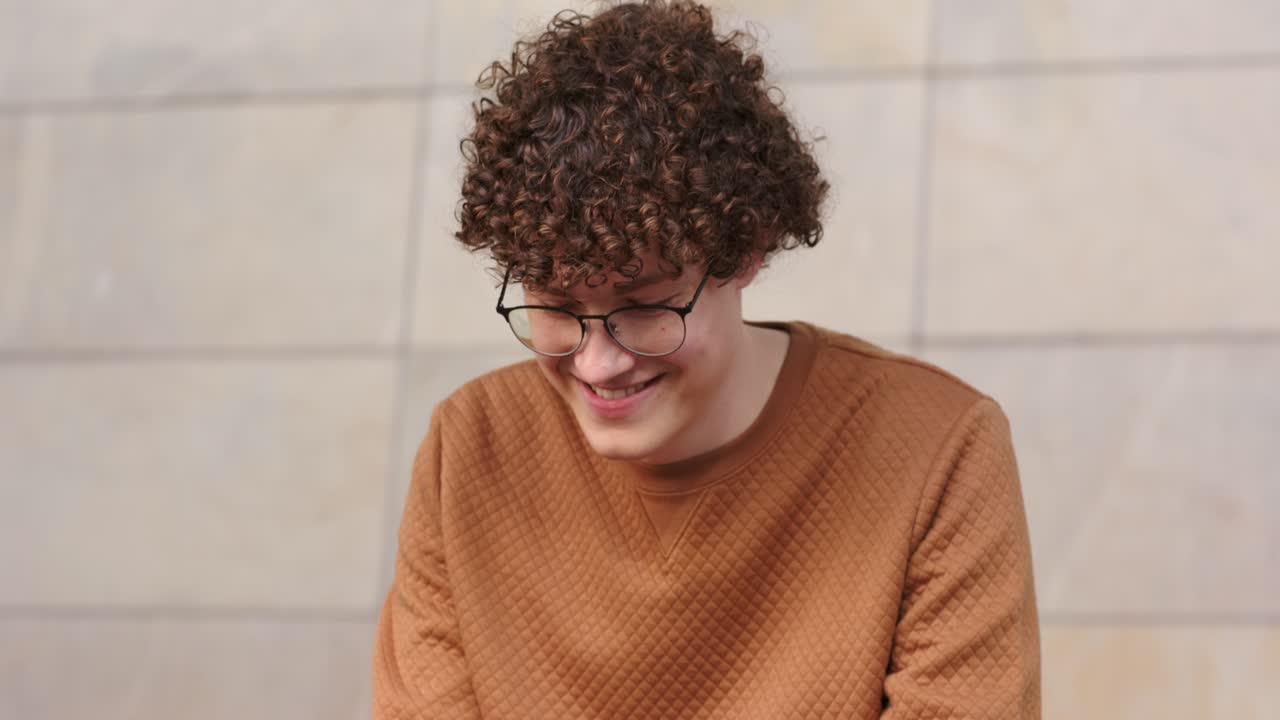 Uomo che tocca lo schermo dello smartphone leggendo un messaggio e sorridendo, guardando alla sua destra su una panchina all'aperto.