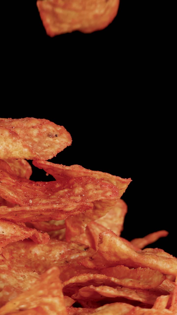 Close-up of hand selecting nacho chip from pile, dramatic lighting, black background, smooth camera rotation