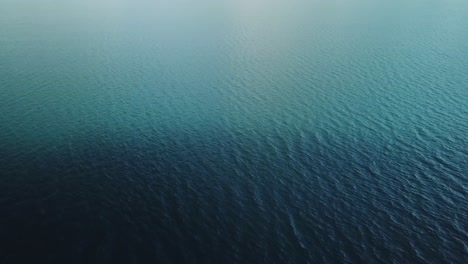 Drone-flight-over-blue-lake-with-different-shades-of-blue