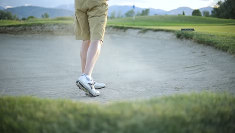 slow motion shot behind a golfer hitting the golf ball out of the sand trap onto the putting green