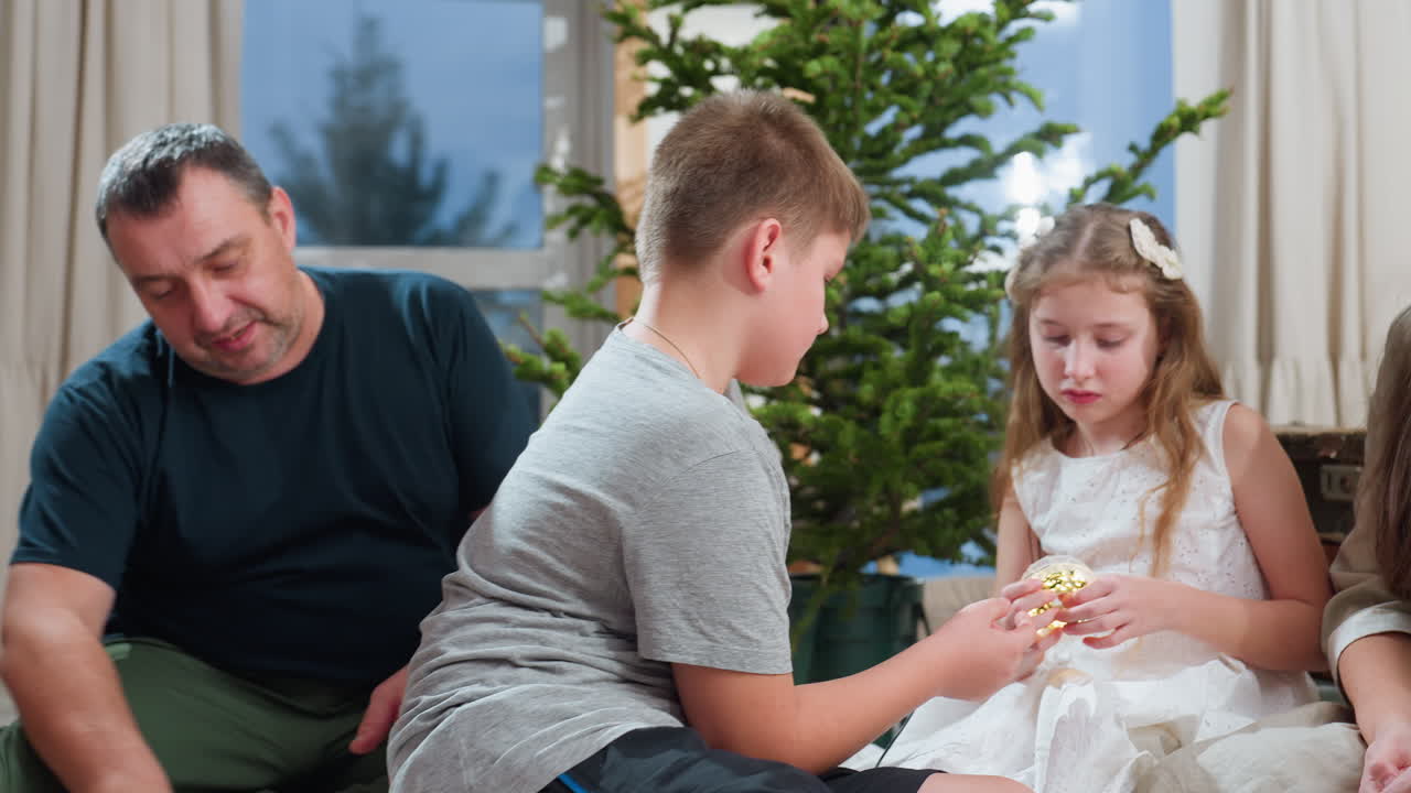 Happy family sitting together with kids playing with wire light in front of Christmas tree, all wearing casual clothes. Cozy atmosphere with festive spirit, showing family bonding moments