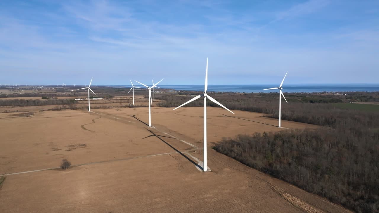 A wind farm on a barren landscape with turbines spinning, coastal line in the distance, aerial view