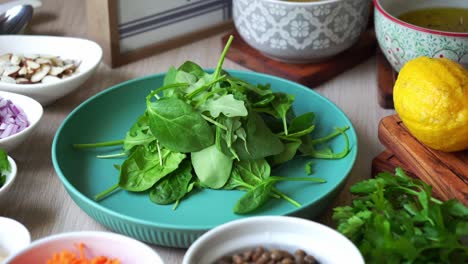 adding salad spinach leaves to plate with ingredients and salad dressing in the background