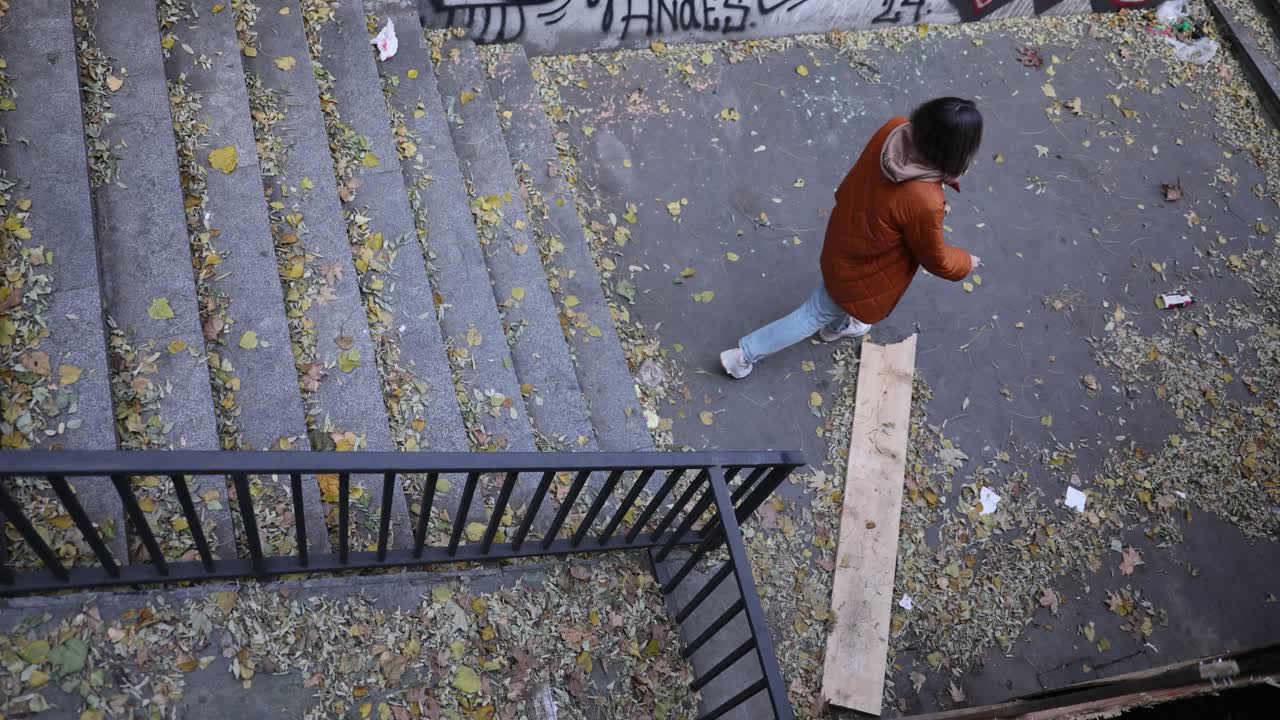 Woman walking down leaf-covered stairs in an urban environment