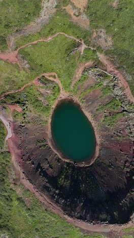 rising top-down drone view of the kerid crater volcanic lake in iceland, vertical video.