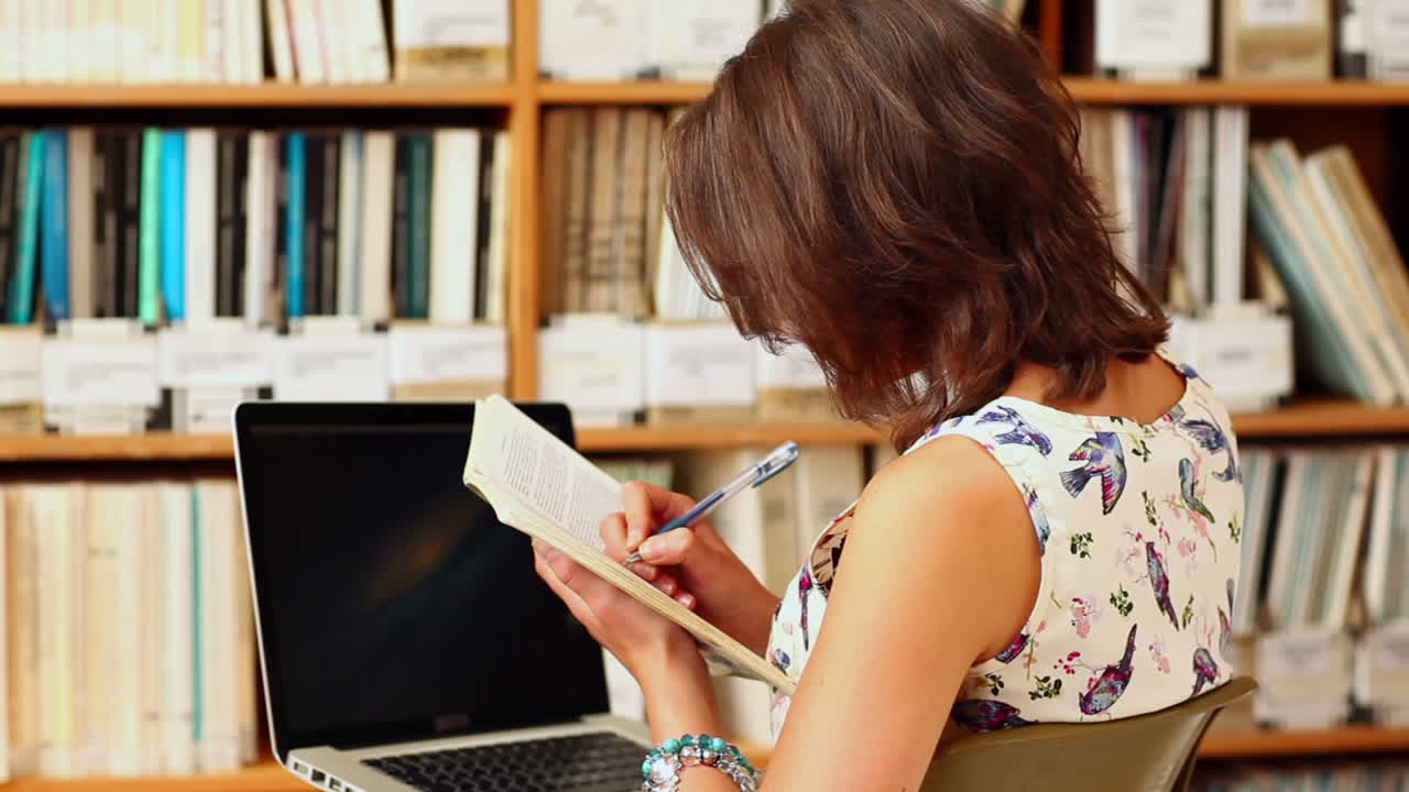 mujer joven estudiando en la biblioteca con una computadora portátil