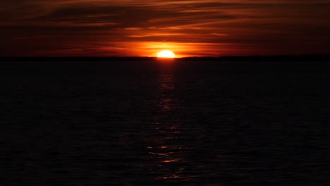 Puesta-De-Sol-Más-Allá-Del-Oscuro-Horizonte-Marino-Ondulante,-Brillando-En-El-Cielo-Oscuro