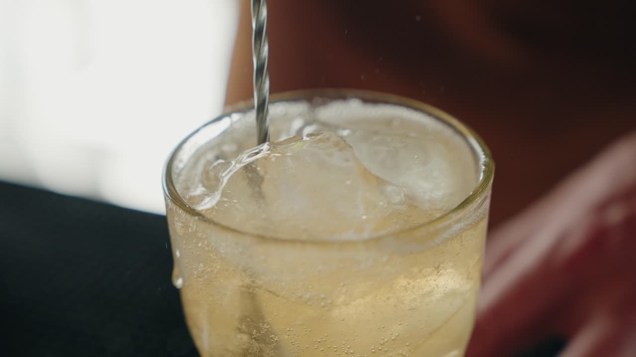 Close up of spoon stirring fizzy drink with ice in glass - slow motion