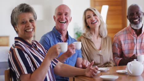 two diverse senior couples sitting by table drinking tea together at home