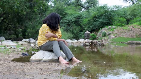 Isolated Girl Sitting Alone on Stone at Calm Lake Shore in the Morning