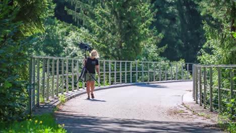 hermosa mujer rubia que lleva equipo de fotografía en medio de la naturaleza