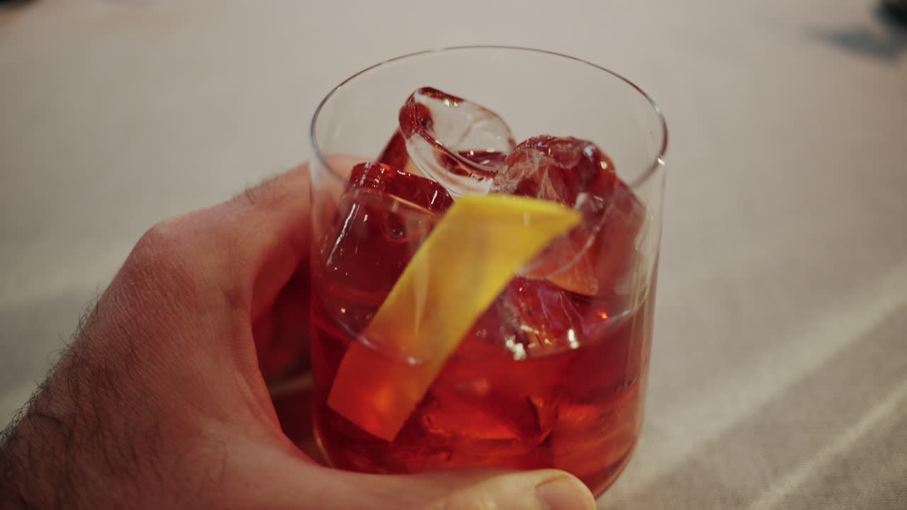 Primo piano di un uomo che tiene in mano un bicchiere da cocktail pieno di ghiaccio e una guarnizione di agrumi