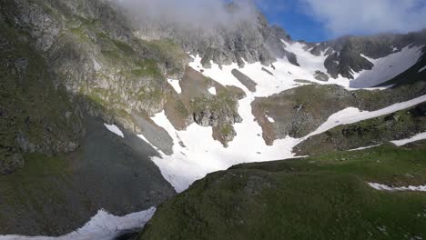 Filmisches-FPV-Drohnen-4K-Luftvideo-über-Gebirgstal-Mit-Schneefelsen-Und-Grünem-Gras-Im-Frühling