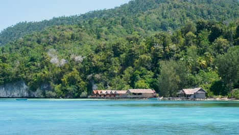 Scenic-landscape-view-of-traditional-wooden-beach-huts-overlooking-ocean-water-on-tropical-island-in-Raja-Ampat,-West-Papua,-Indonesia