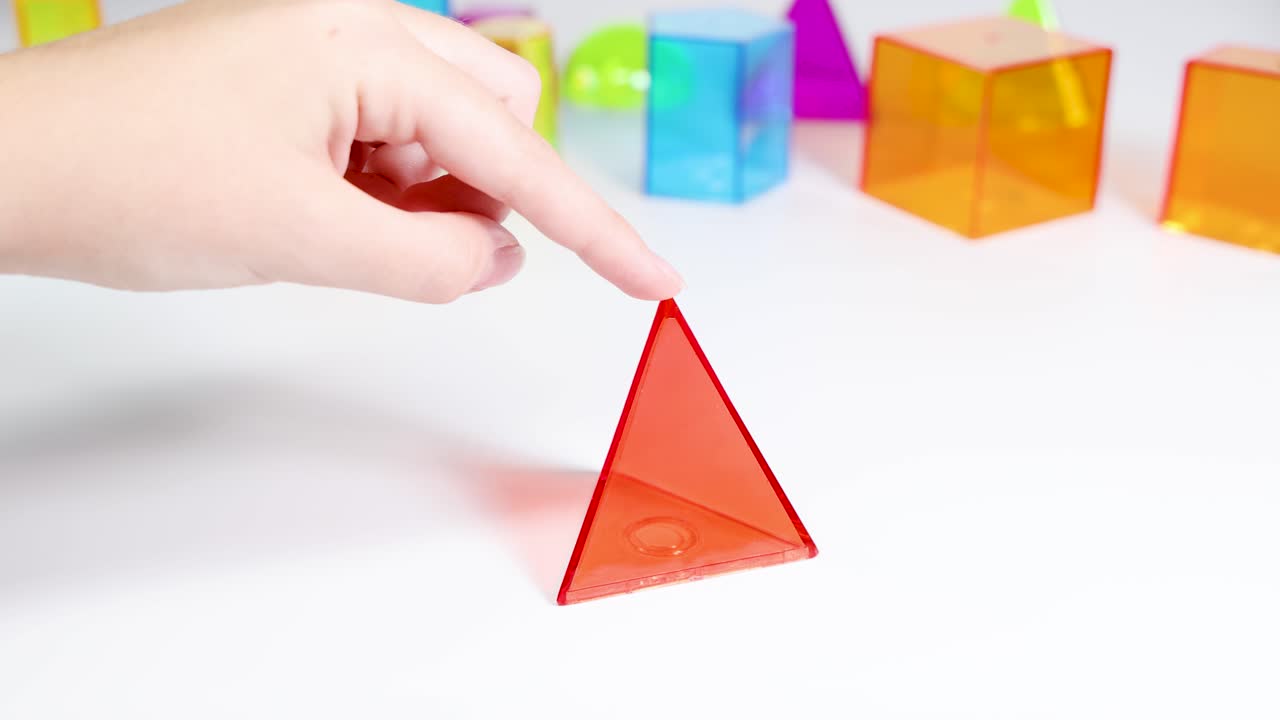 Hands manipulate vibrant 3D shapes on a white surface, demonstrating movement and interaction in a bright, educational setting