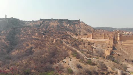 Wide-panoramic-over-the-barren-hills-surrounding-the-Amber-Fort-in-Jaipur,-Rajasthan,-India---Aerial-Panoramic-orbit-shot