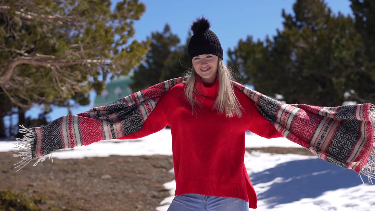 Blonde Frau genießt die verschneiten Berge, hebt die Arme und spielt mit ihrem Schal in Zeitlupe.