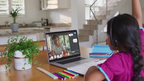 Schoolgirl-using-laptop-for-online-lesson-at-home,-with-female-teacher-and-web-chat-on-screen