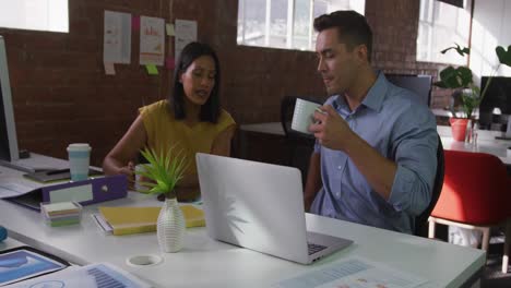 Diverse-male-and-female-business-colleagues-in-discussion-at-work-drinking-coffee-and-smiling