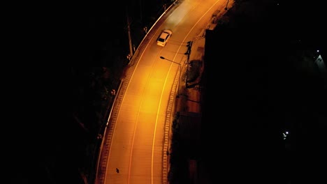 Toma-Aérea-De-Un-Camión-Blanco-Conduciendo-Por-Una-Carretera-Vacía-Por-La-Noche-En-Una-Zona-Rural-Con-Luces-Amarillas-En-La-Calle