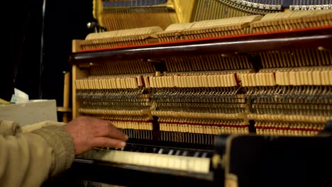 hands of old man in subway underground playing piano with opened mechanism og strings and hammers