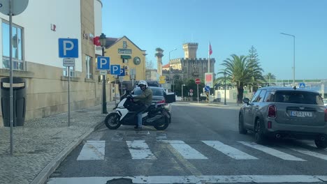 hombre con casco blanco sentado en una moto y hablando por teléfono en la calle de buhardilla en estoril, cascais