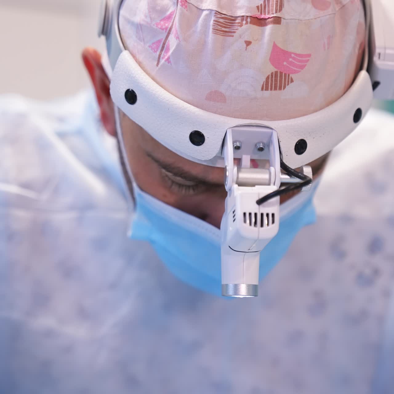 Head of a surgeon in cap and device glasses bent over the patient. Portrait of a male doctor busy with his responsible work