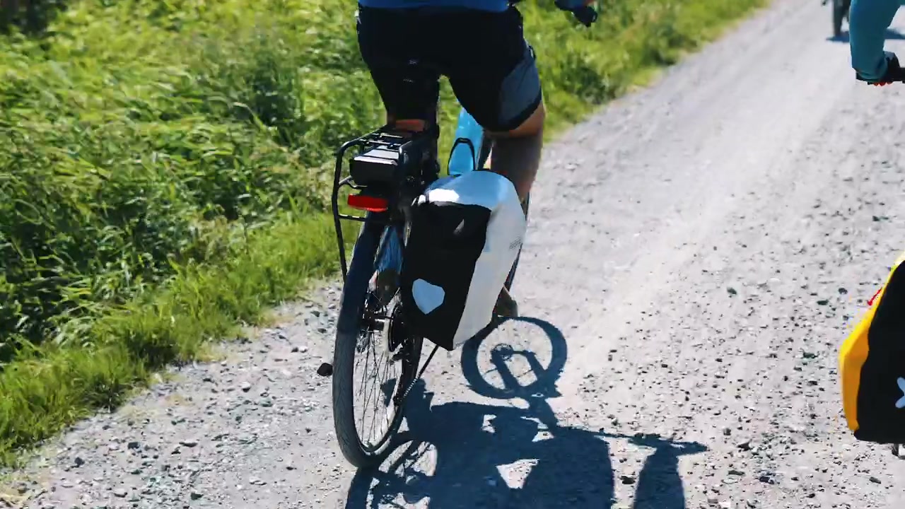Close-up de um Ciclista Pedalando com Alforjes Traseiros numa Bicicleta de Cicloturismo pela Rota de Cascalho EuroVelo 10 na Paisagem Rural Dinamarquesa num Dia de Verão Ensolarado