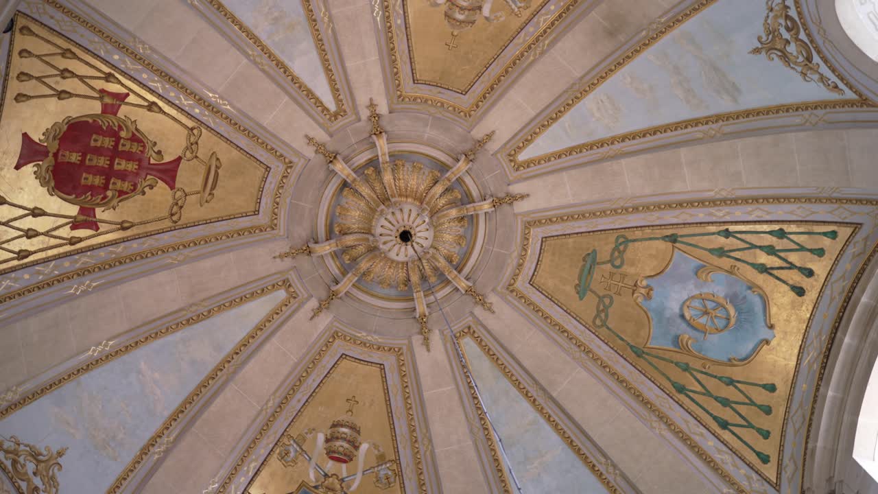 Upward view of an ornate church dome ceiling decorated with gold details and heraldic shields