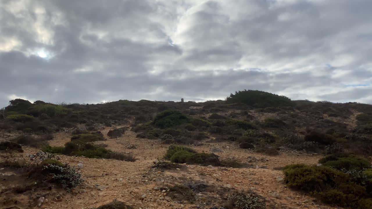 A winding valley cuts through sandy and rocky Algarve terrain beneath a misty morning sky, full of quiet strength