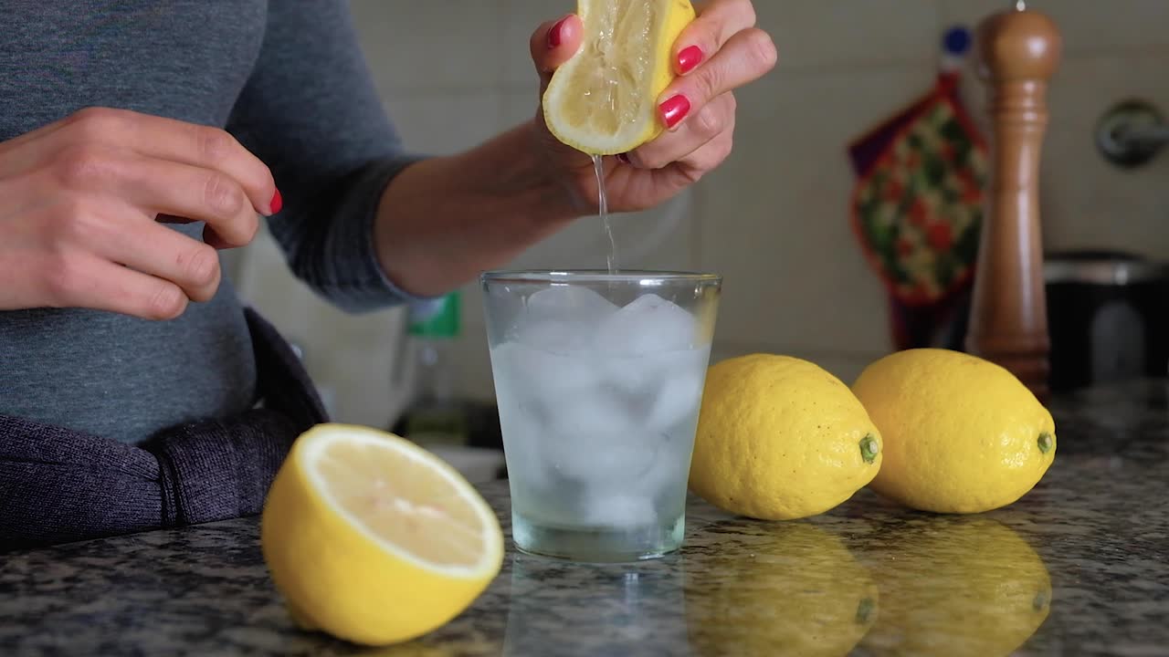 Cámara lenta de una mujer exprimiendo un limón en un vaso con agua y cubitos de hielo