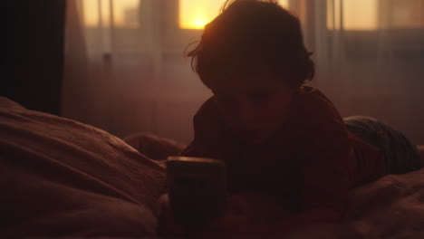 child using smartphone in bed at sunset