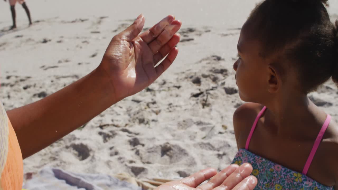 familia afroamericana sonriente usando crema solar en una playa soleada