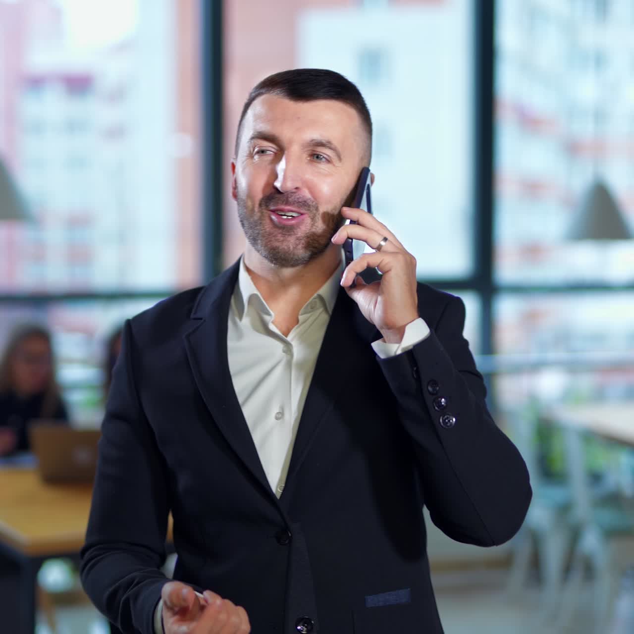Confident self-sure relaxed businessman speaks on the phone in office. Teammates at the desk at background in blur