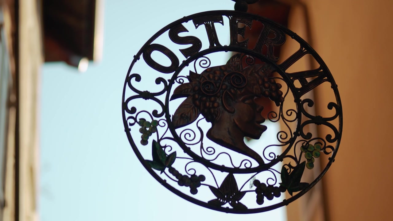 Insegna vintage in metallo di un'osteria all'aperto con silhouette del profilo di Bacco in una storica strada italiana