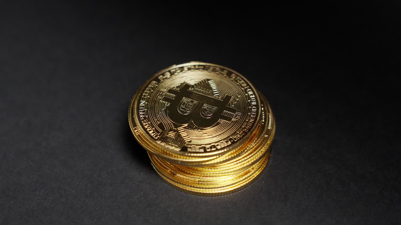 Hand takes a shiny Bitcoin coin from a stack on black background, concept of value