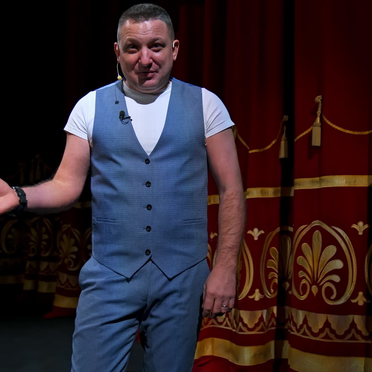 Showman entertains the audience under the light, front view. Big stage. Funny performer speaks to the camera. Active gestures on a stage