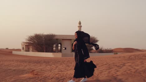 mujer musulmana de pie cerca de la mezquita en el desierto. viento fuerte oriente medio paz sin guerra