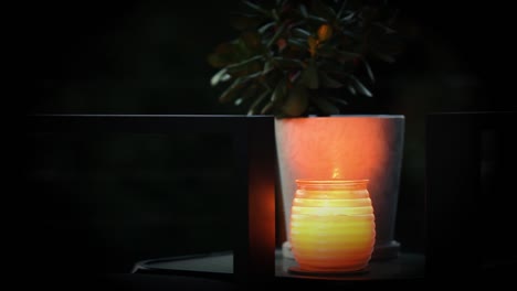 Flickering-candle-on-side-table-with-green-succulent-plant-growing-along-side