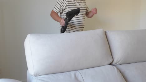 Panning right shot of a cleaner man behind the sofa in the living room with a special cleaning machine