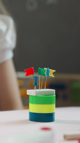 la niña construye una torre con borrador y pequeñas banderas en la parte superior del escritorio en el aula de primer plano. la estudiante se divierte con papelería de color en la lección de artesanía